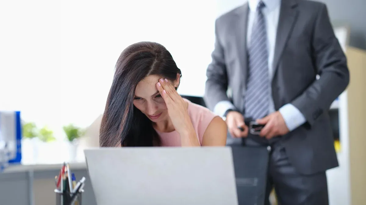 Une femme effrayée est assise à l'ordinateur en arrière-plan. Un homme d'affaires détache sa ceinture.