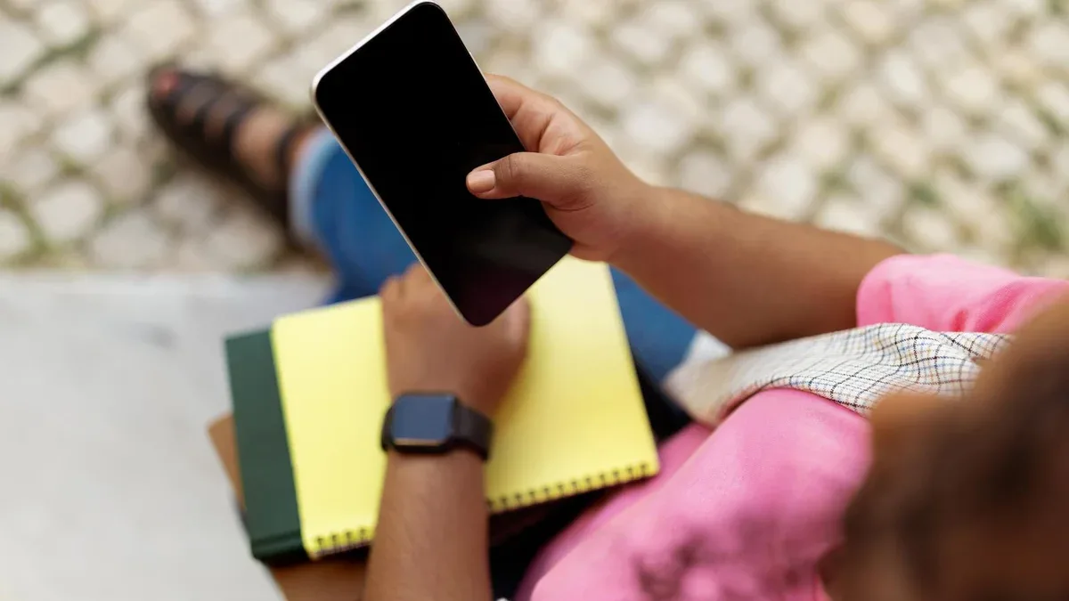 Personne assise sur les marches en utilisant un smartphone tout en tenant un bloc-notes et un stylo