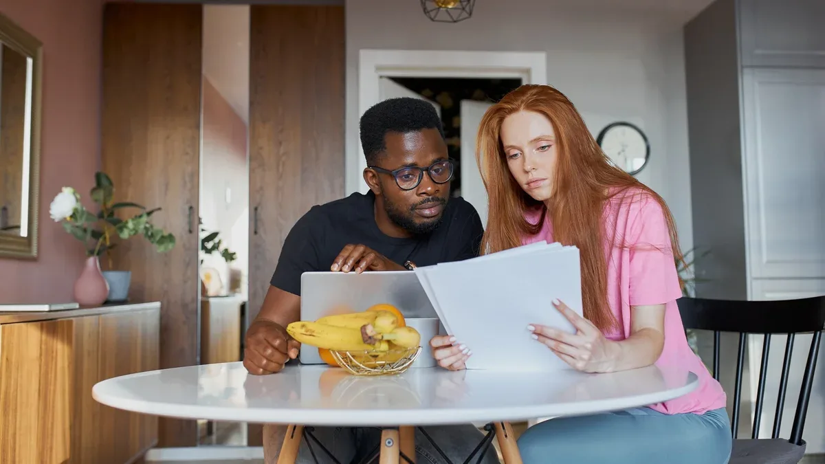 Homme africain sérieux lire des papiers et femme de race blanche discuter des factures internes impayées